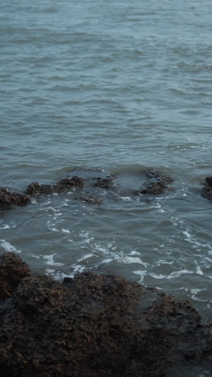 Gentle waves lap against rocky formations in a calm seaside scene, vertical shot