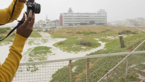 side view of young black man clicking photo of woman with digital camera on promenade at beach 4k