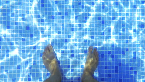 male feet in clear water of the pool