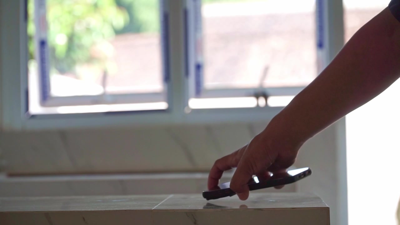 Person picking up a smartphone from a table indoors. Mobile technology, communication, connectivity, and everyday lifestyle concept.