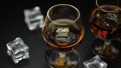 two glasses of brown liquor with ice on a black background