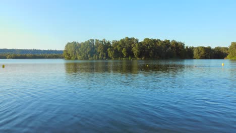calm lake landscape with tree-covered island and distant swimmer