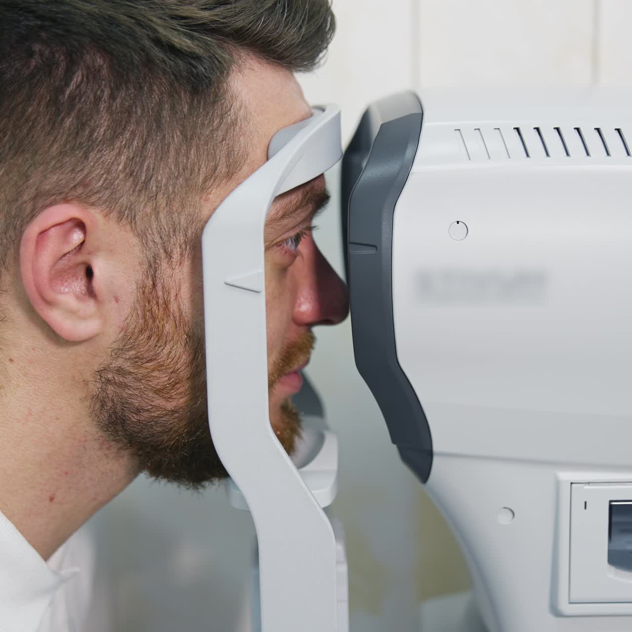Patient man looks at device in ophthalmology clinic. Profile of patient's face looking into apparatus for eyes diagnostic in clinic. Close-up