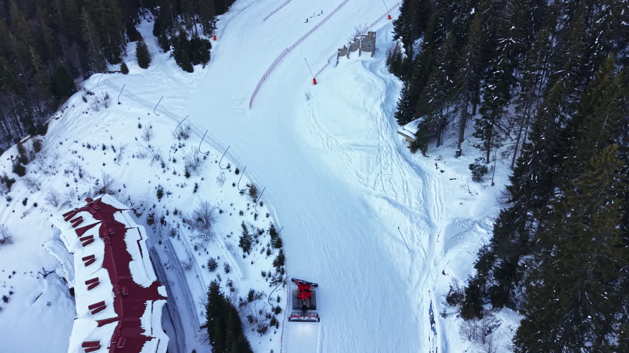 Scena sciistica invernale su un pendio innevato in montagna in una giornata limpida, con persone che sciano e fanno snowboard in lontananza vicino a un rifugio.
