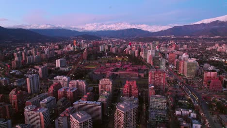 Drone-Aéreo-Sobre-La-Estación-De-Metro-De-Santiago-Chile-Escuela-Militar-Fondo-De-La-Cordillera-Andina-En-El-Horizonte-Rosa-Y-Azul,-Tiro-De-Establecimiento-De-Ciudad-Latina