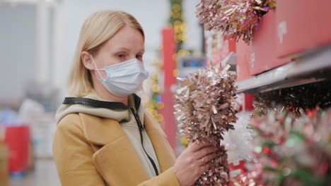 the masked buyer chooses garlands and decorations for the christmas tree. shopping during the coronavirus pandemic