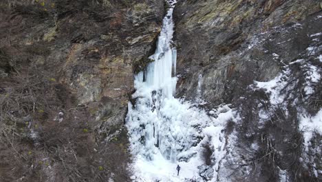 Aerial-view-of-woman-walking-towards-a-frozen-waterfall