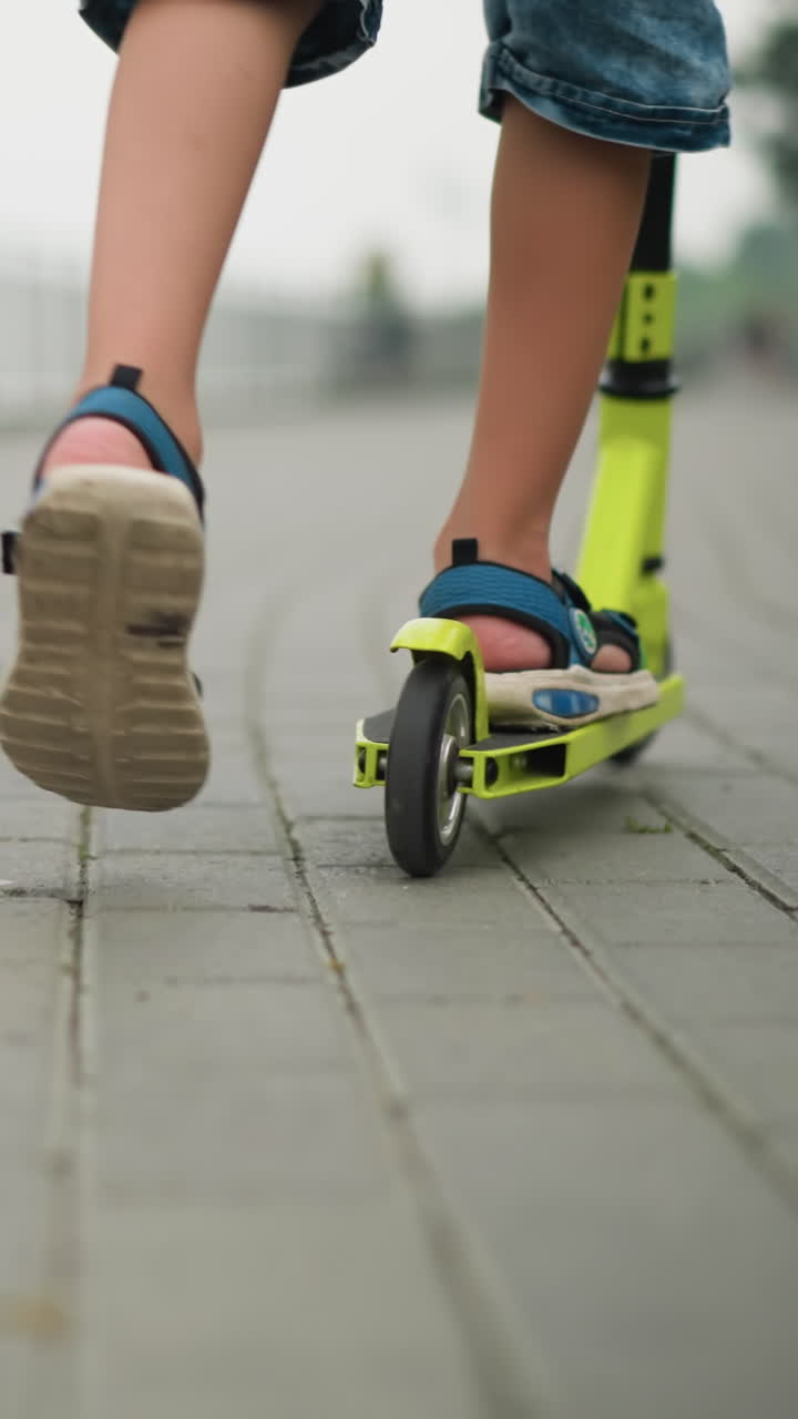 Close-up of a child and a woman riding scooters side by side, the child rides a green scooter, while the woman is on a black one