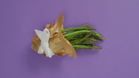 Video-of-fresh-asparagus-wrapped-with-white-ribbon-and-copy-space-over-lilac-background