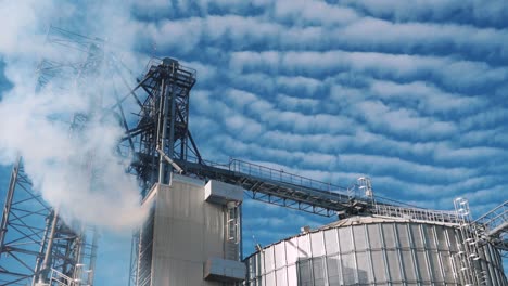 white smoke from the factory chimney. environmental pollution. large metal structures of the elevator on the background of the sky with clouds. storage and drying of grain