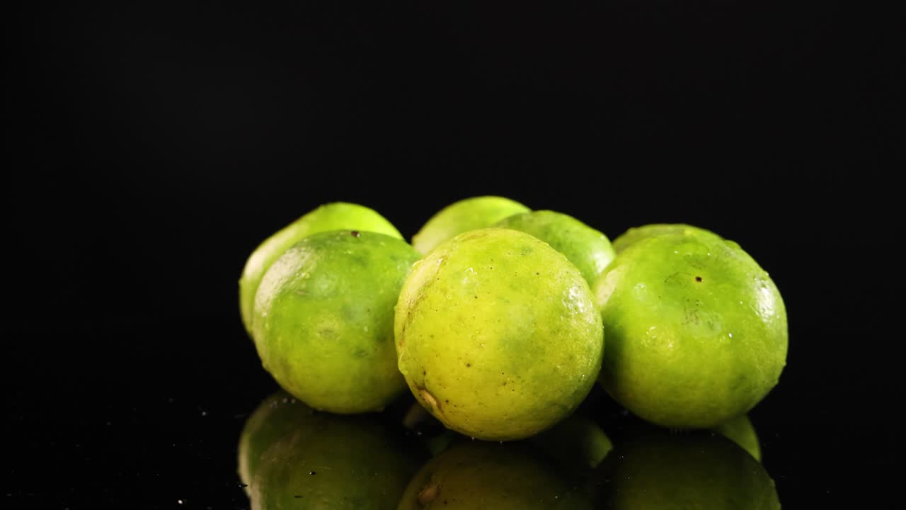 Limes rotate smoothly on a reflective black surface, highlighting their vibrant green color and texture under bright lighting