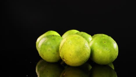 limes rotate smoothly on a reflective black surface, highlighting their vibrant green color and texture under bright lighting