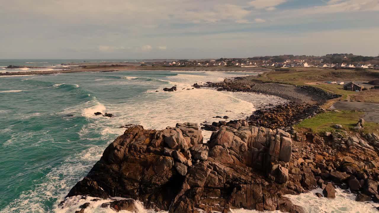 Low flight over rocky shoreline with crashing white foaming waves rolling onto shore and into bays on a bright but windy afternoon in Guernsey