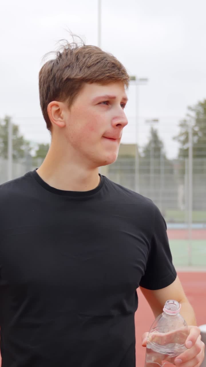 Young man drinking water on sports field after workout, hydration, fitness, self-improvement and healthy lifestyle