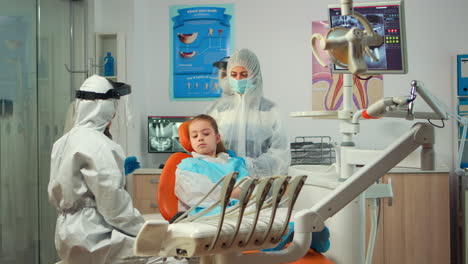 stomatologist in ppe suit holding plaster model of the mandible speaking with girl