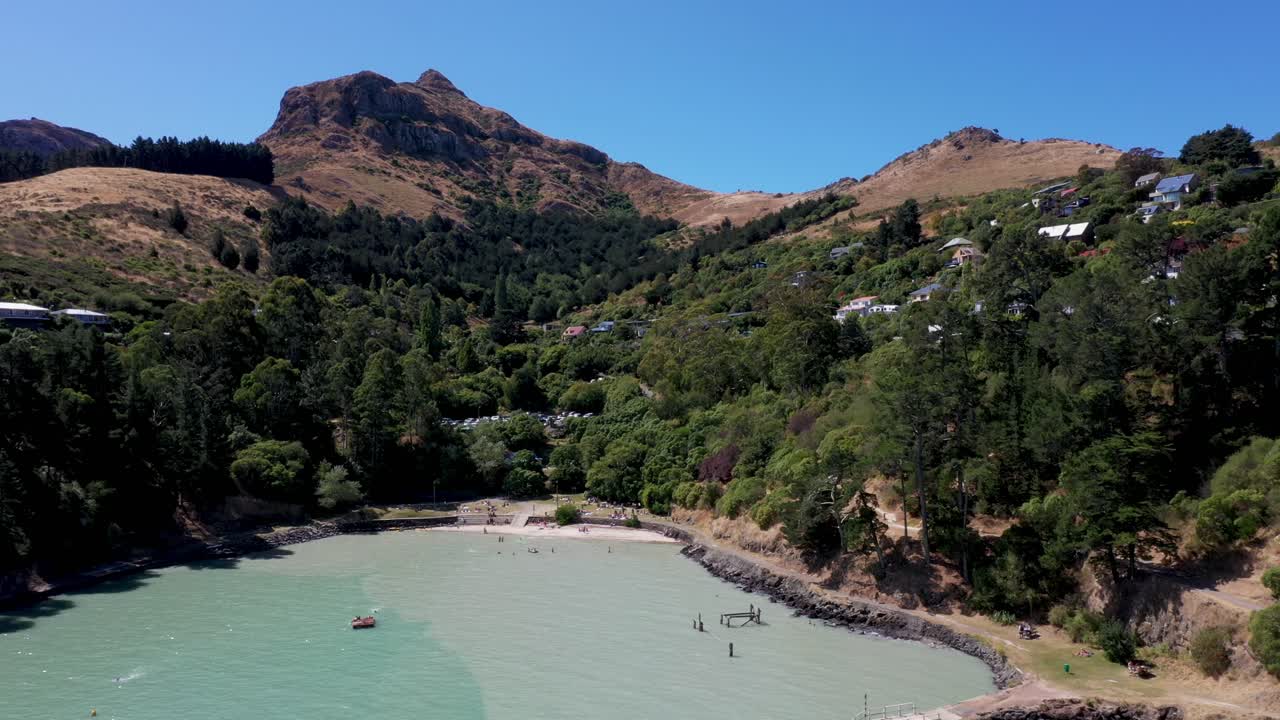 Tracking and panning aerial shot of pretty bay with pine trees and rocky mountain in background