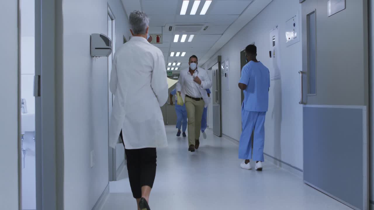 Diverse group of male and female doctors in face masks running through hospital corridor