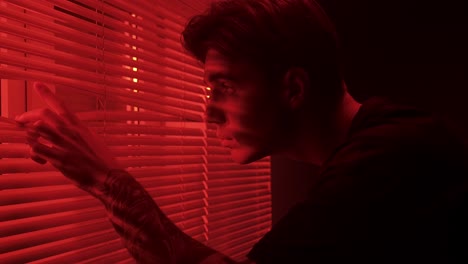 man looking through red lit blinds