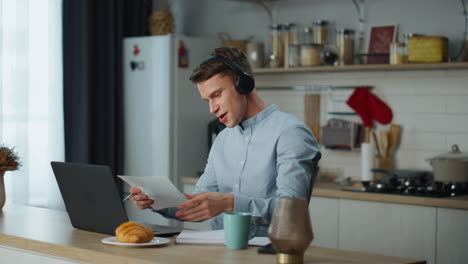 trabajador remoto escuchando música desde auriculares trabajando en la cocina de casa usando una computadora portátil.