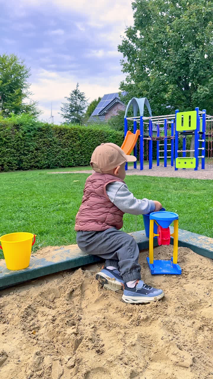 Child joyfully playing in a sandpit on a sunny afternoon in a park with playground equipment nearby