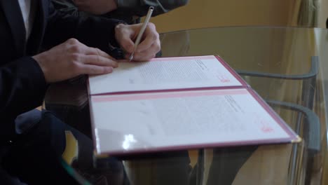 Witnesses-Of-The-Groom-And-The-Bride-Who-Sign-The-Town-Hall-Register-in-slowmotion-on-a-glass-table-ceremony-civil