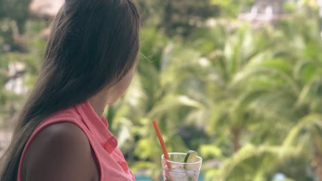 girl stands on balcony with mojito and looks away at palms