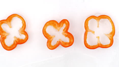 Splashes-of-water-fall-on-sliced-red-pepper-rings-on-a-white-background