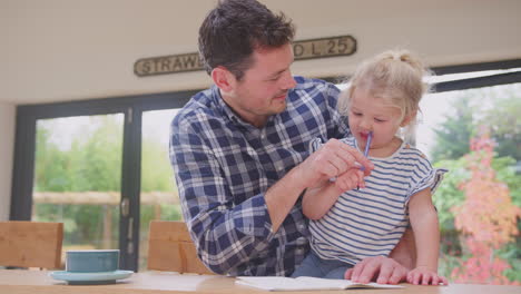 padre en casa en el mostrador de la cocina ayudando a su hija a dibujar en un libro - filmado en cámara lenta