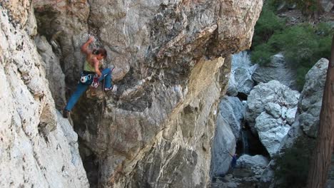 longshot of a rock climber rearranging her carabineers to climb a cliff wall