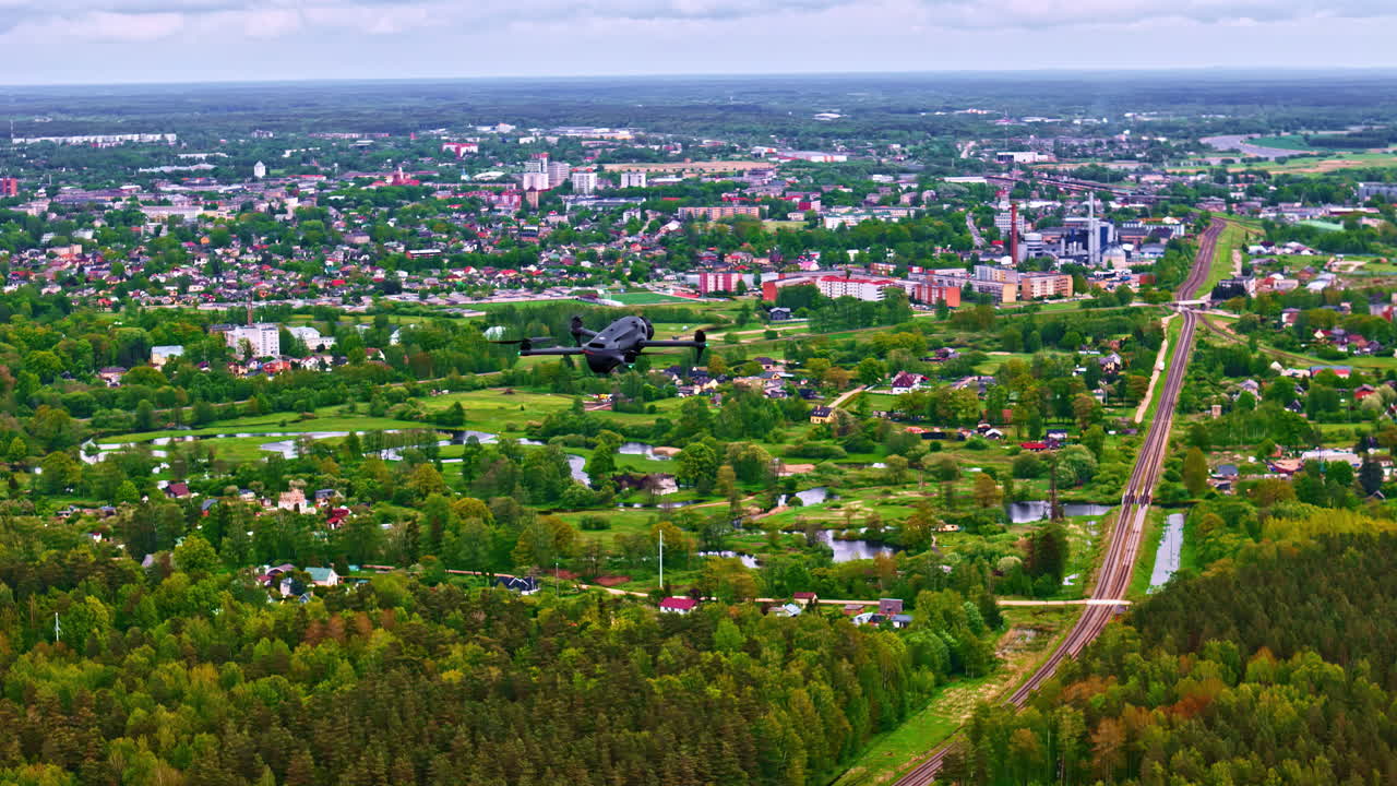 Aerial shot of a drone hovering over a landscape with green forests and a city.