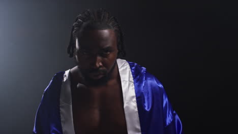 portrait of boxer wearing robe entering ring and warming up before start of boxing match with low key lighting