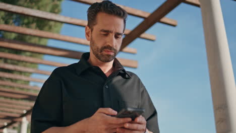 hombre relajado caminando por la calle de la ciudad de verano sosteniendo un teléfono inteligente en primer plano.