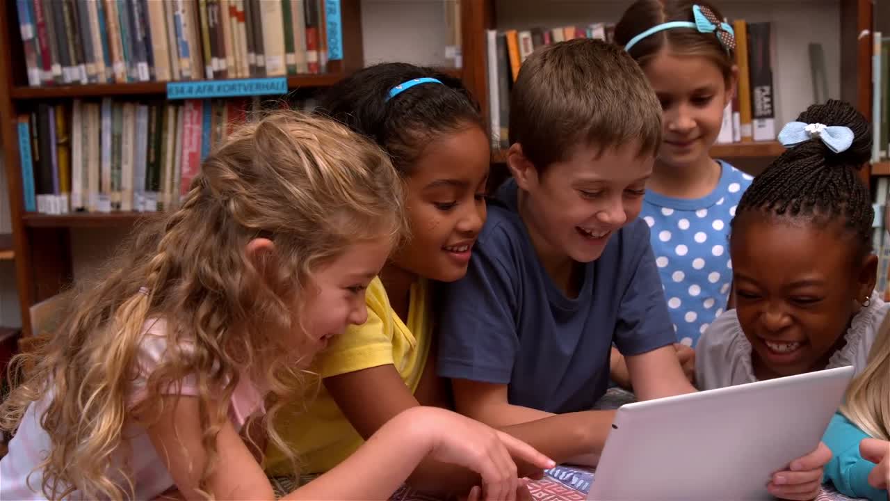 Cute pupils looking at laptop in the library