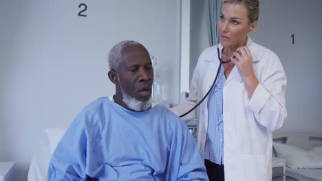 caucasian female doctor examining african american senior male patient with stethoscope at hospital
