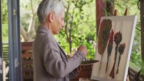 Portrait-of-senior-mixed-race-woman-painting-and-smiling-on-balcony