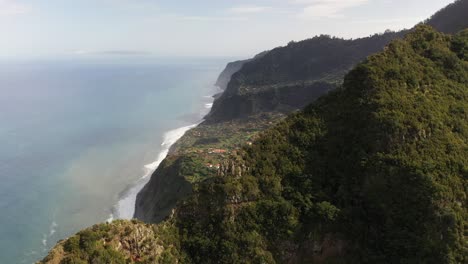 Drone-shot-flying-over-a-mountain-top-to-reveal-the-landscape-and-valley-below-with-a-small-village-in-Madeira