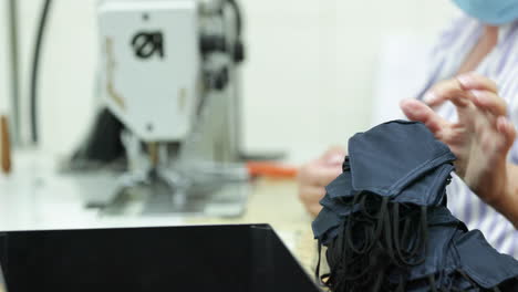 a seamstress setting aside the final product of blue face masks in a sew factory - covid-19 pandemic - rack focus shot pan right