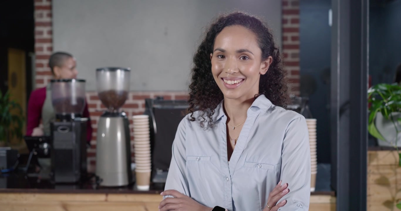 Mulher afro-americana caminhando da direita para o balcão, pedindo café enquanto o barista usa o moedor.