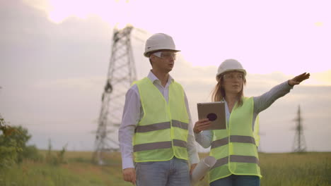 Ingenieros-Uniformados-Trabajando-Con-Una-Computadora-Portátil-Cerca-De-Líneas-De-Transmisión.