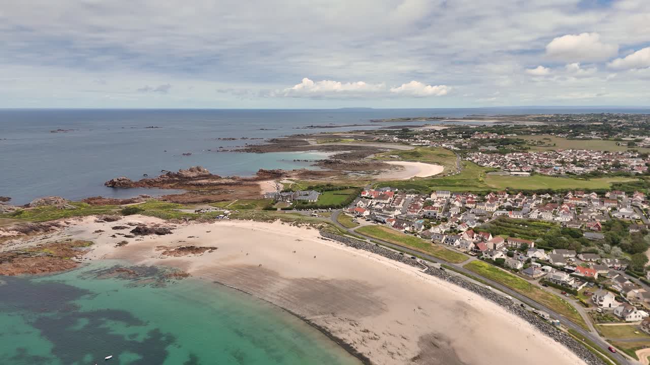 Guernsey.High drone flight over successive beautiful bays with golden beaches on West coast of Guernsey and boats at anchor in calm clear turquoise sea and rocky foreshore on bright sunny day