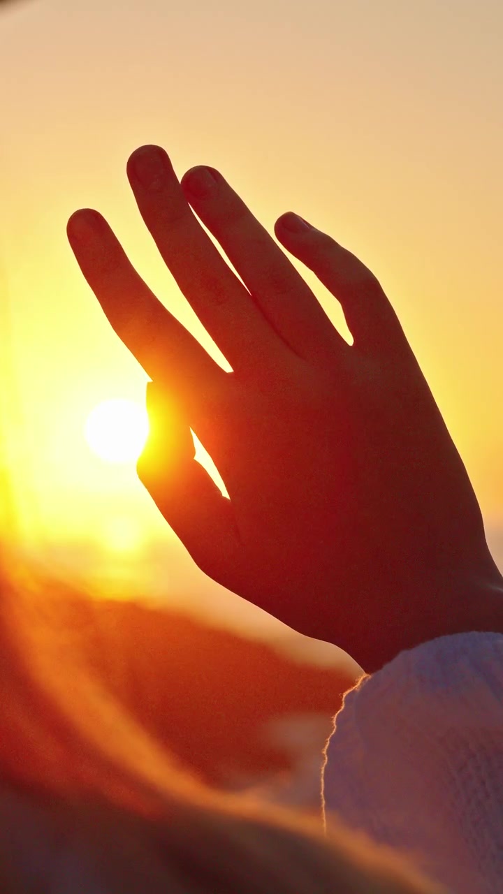 Mano alzata che incornicia il tramonto tra le dita