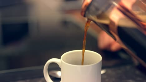el café caliente al vapor se vierte de una jarra de vidrio en una taza blanca brillante