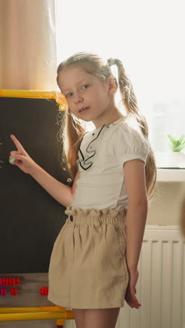 girl explains mathematics to boy pointing to problems on blackboard slow motion. couple of children play school at home. brother and sister study together