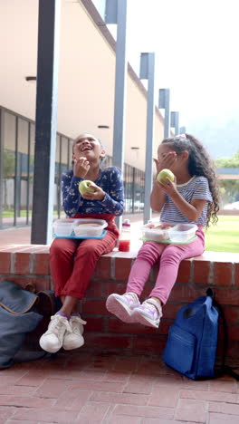 vertical video: in school, two young biracial girls are enjoying lunch