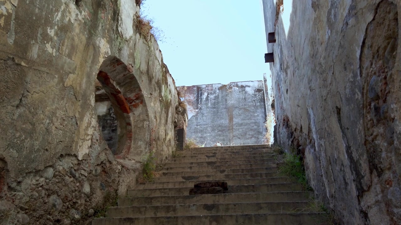Antica scalinata in pietra conduce a un cielo luminoso in un contesto di rovine storiche.