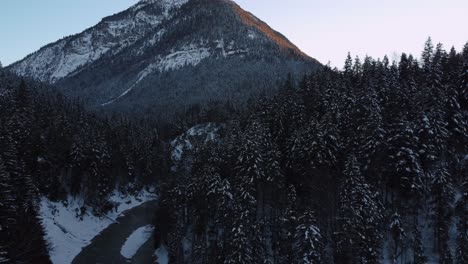 Volando-Hacia-Una-Enorme-E-Impresionante-Montaña-Con-Bosques-Y-árboles-En-Invierno-Con-Nieve-Y-Hielo-En-Las-Idílicas-Y-Escénicas-Montañas-De-Los-Alpes-Austriacos-Bávaros-Con-Picos-Rojos-Al-Atardecer