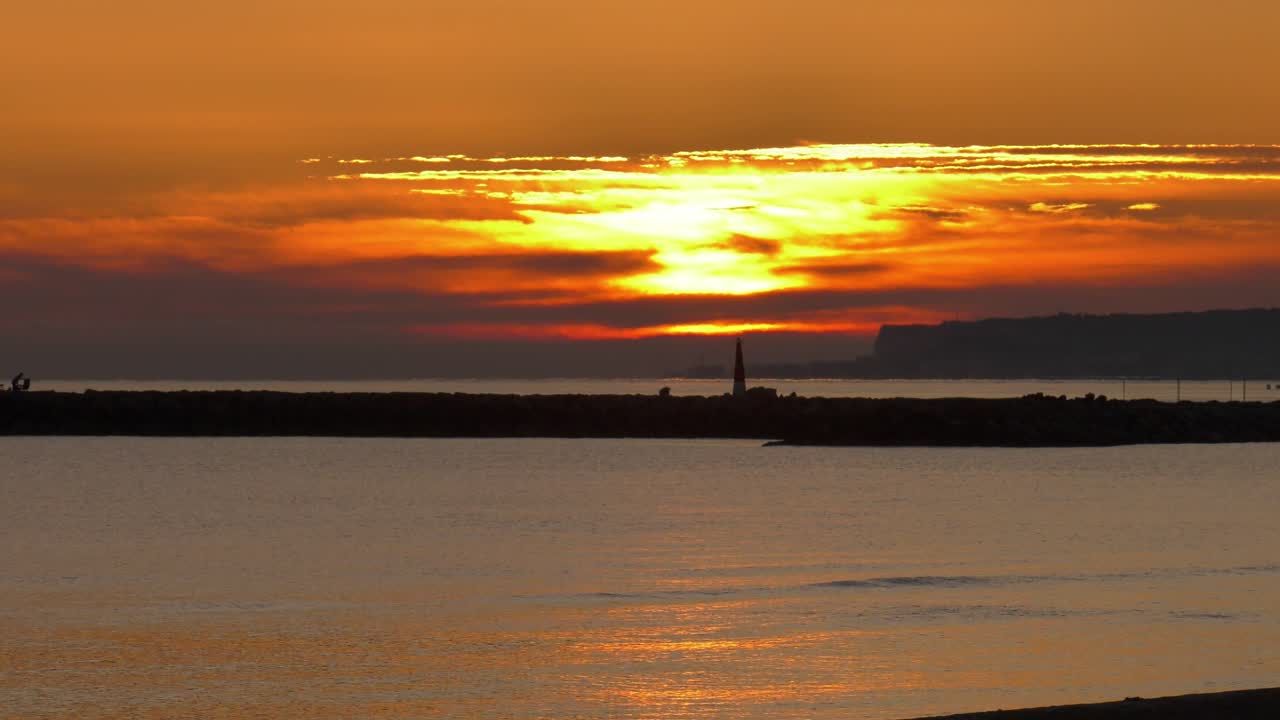 Clouds cover sun rising over calm sea with harbor wall