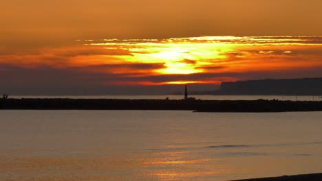 clouds cover sun rising over calm sea with harbor wall