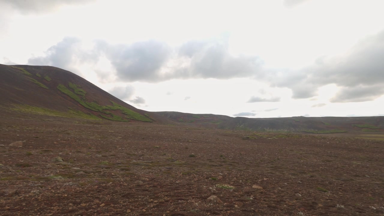 Dataran lava tandus di bawah kerucut vulkanik di Fagradalsfjall Islandia, dengan pengambilan gambar panorama ke kiri.