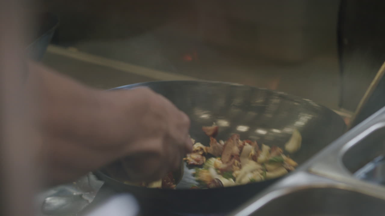 Wok dish is baked in a pan. There is a lot of fire to be seen. The pan is turned and the food flies around. The footage is in slow motion.